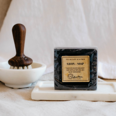 Black Lothantique bar soap in clear packaging. Displayed on marble soap tray. 