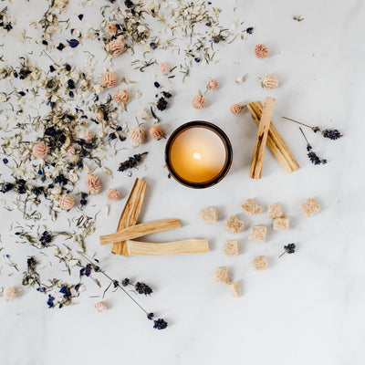 Flat lay of Lolly candle featuring dried lavender, dried pink flowers, raw sugar cubes, and palo santo sticks. 