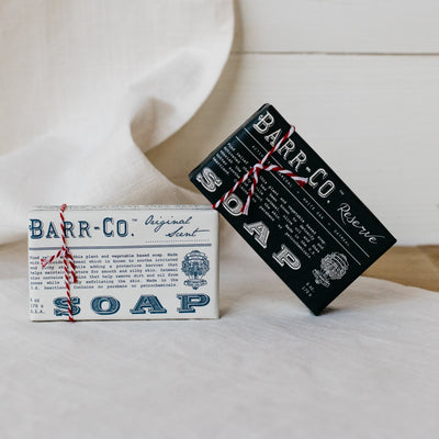 Barr Co Original scent bar soap in class ivory paper packaging and Barr Co reserve scent bar soap in classic black paper packaging