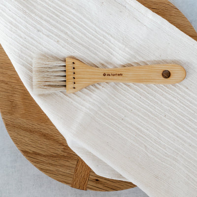 Iris pastry brush displayed on wooden culinary board with white linens.