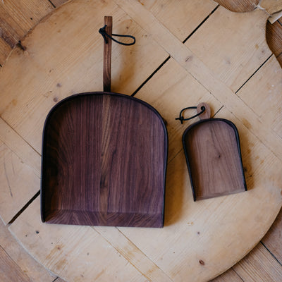 Regular and child-size leather and walnut dustpans displayed on vintage wooden board. 