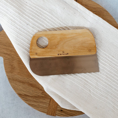 Iris dough scraper displayed on wooden culinary board with white linens. 