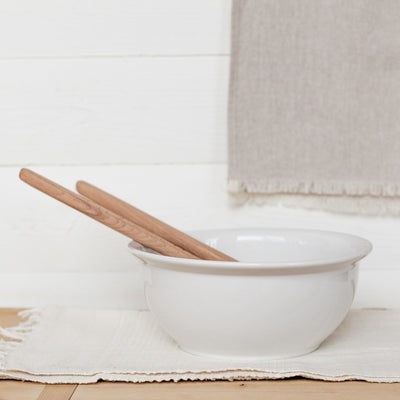 White stoneware kitchen bowl displayed with wooden spoons. 