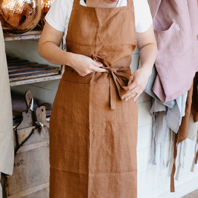 Modeled linen bib apron in cinnamon, tied with a bow in the front.