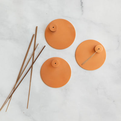 Round copper incense holders displayed with incense sticks. 